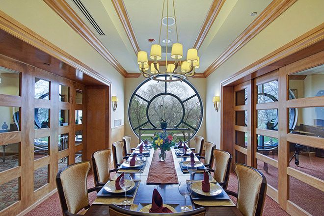 An elegantly set dining room with a large circular window and a chandelier overhead.