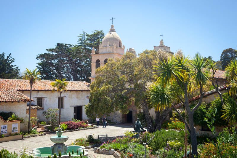 A historic mission building with a garden and fountain in California.