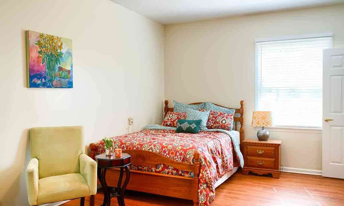 A cozy bedroom with a floral bedspread, wooden furniture, and a window letting in natural light.