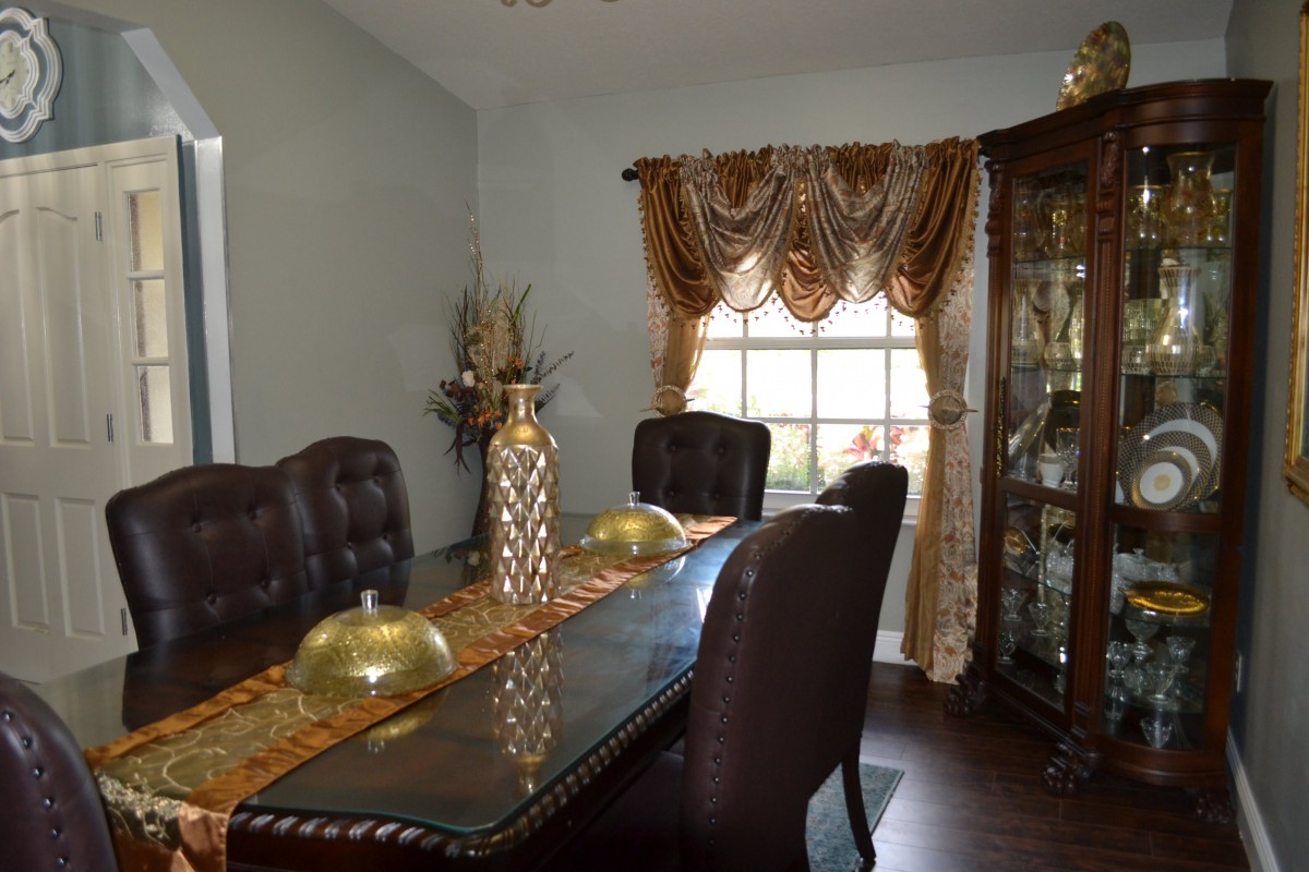 A stylish dining room with elegant furniture and decorative accents, featuring a large window with ornate curtains.