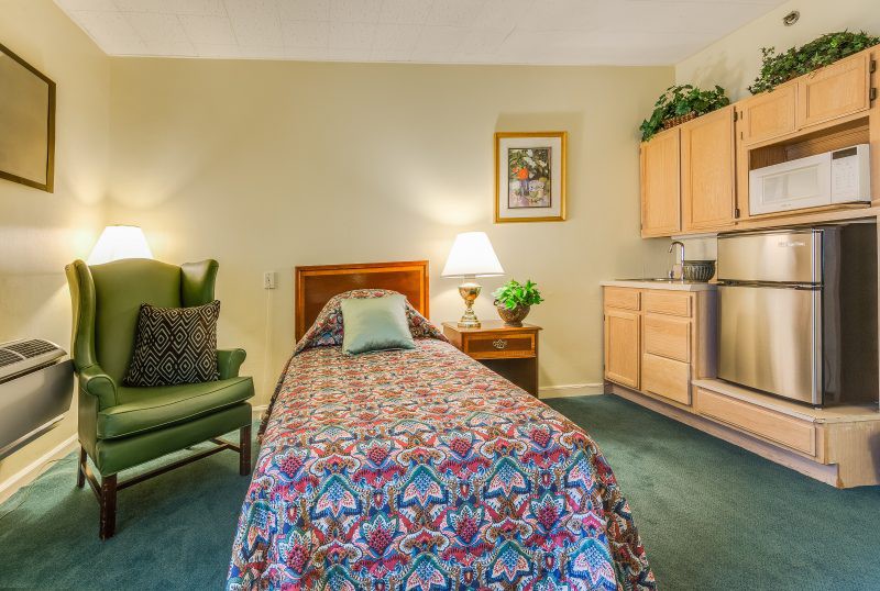 A cozy bedroom with a single bed, armchair, and warm lighting.