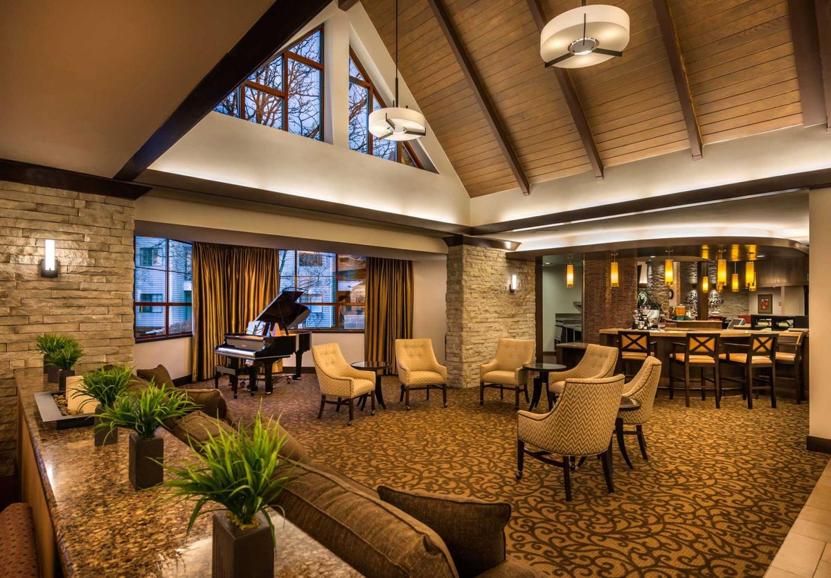 A modern hotel lobby featuring a grand piano and comfortable seating arrangements under warm ambient lighting.