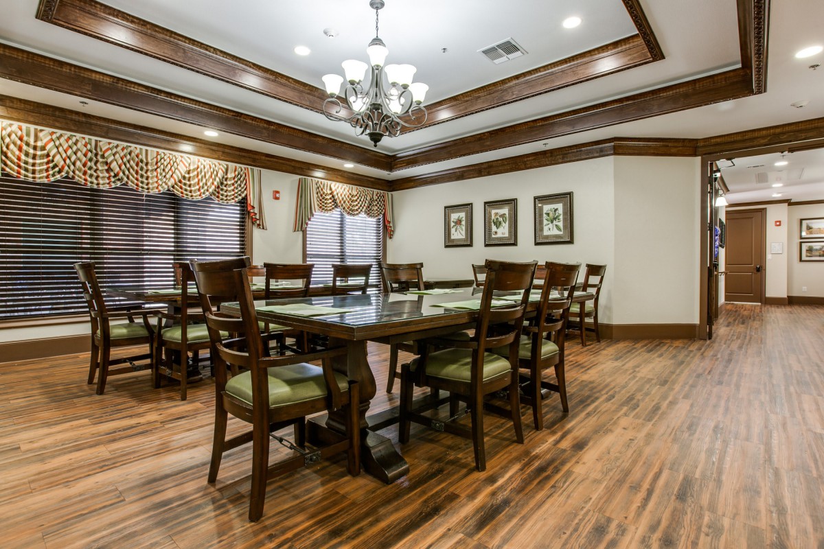 A spacious dining room with traditional decor, featuring a large wooden table and chairs, elegant chandelier, and wood flooring.