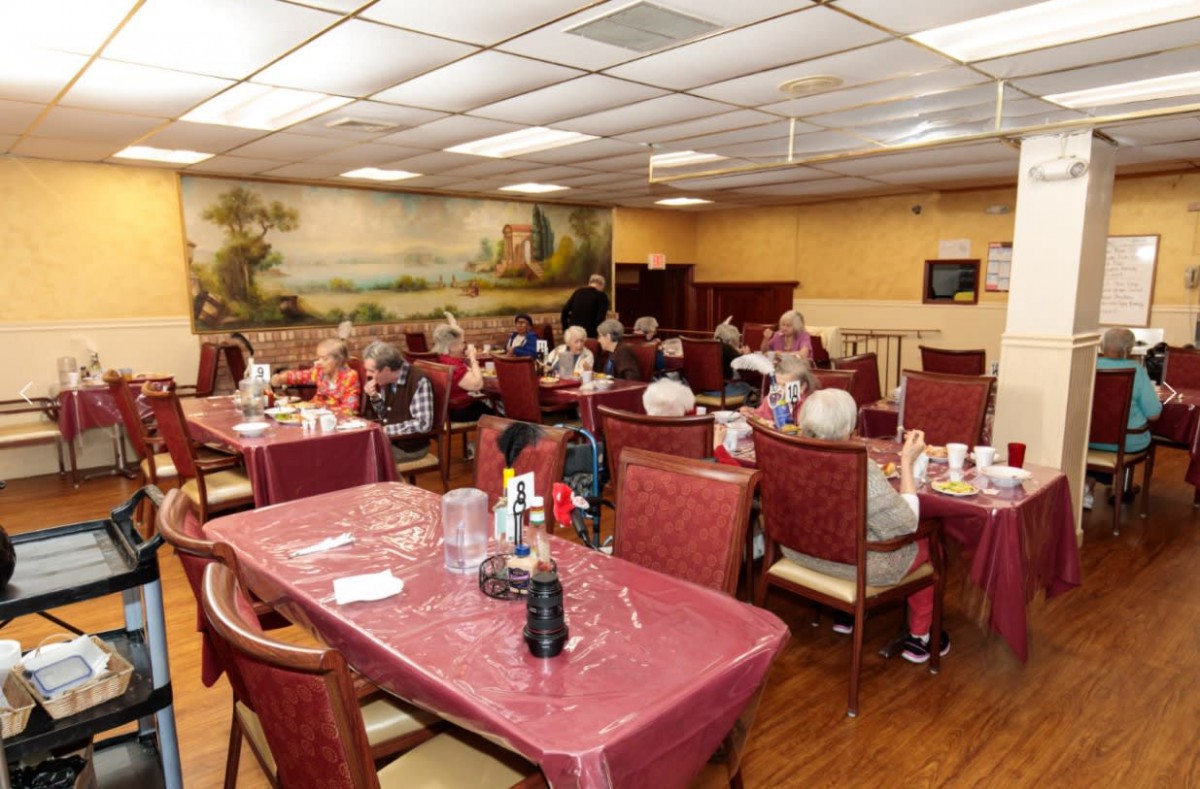 A busy restaurant interior with patrons dining at tables covered in maroon tablecloths.