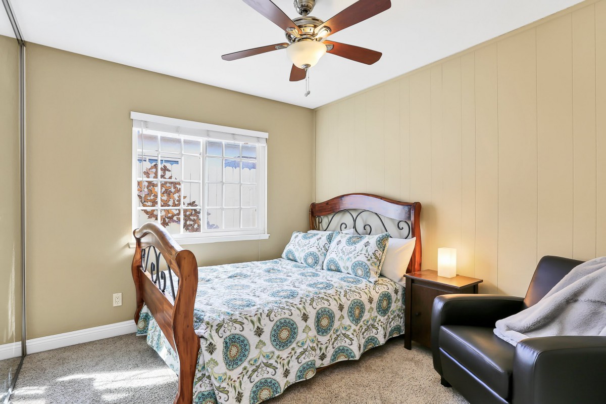 A cozy bedroom featuring a wooden bed with patterned bedding, a bedside lamp, and a ceiling fan.