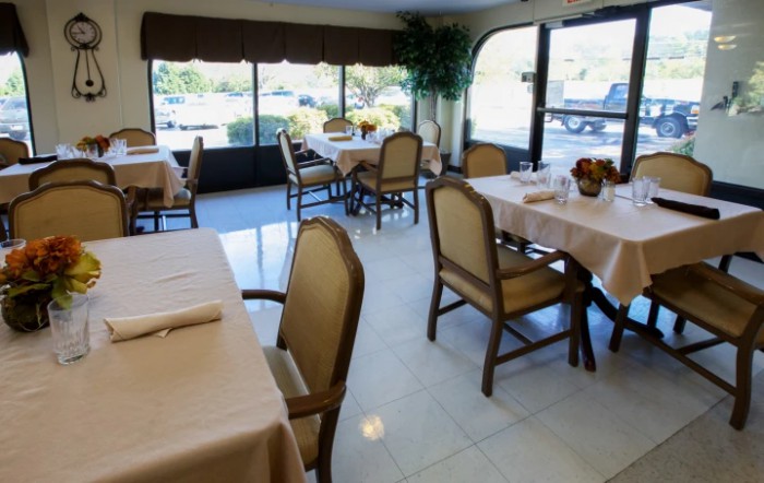 A cozy restaurant interior with neatly arranged tables and chairs, illuminated by natural daylight coming through large windows.