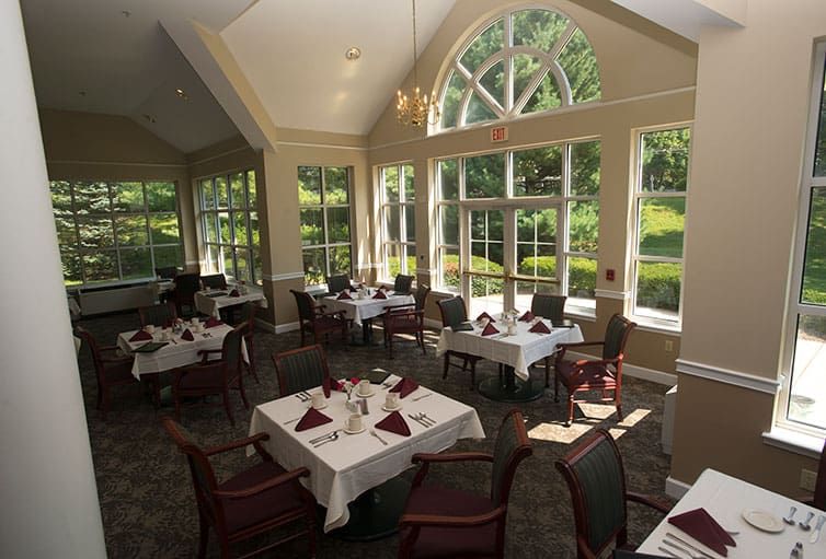 A spacious dining room with elegantly set tables and large windows letting in natural light.