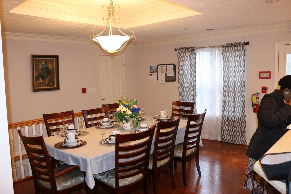 A neatly set dining room with a large table, chairs, and a chandelier above.