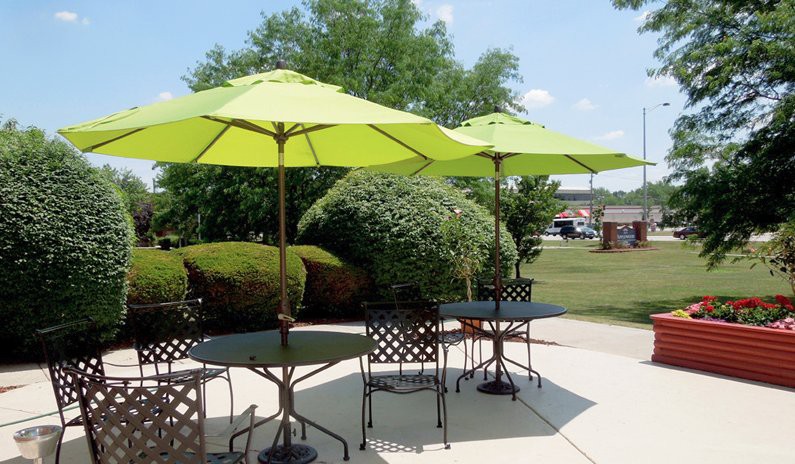 Outdoor patio area with green umbrellas and metal furniture on a sunny day.