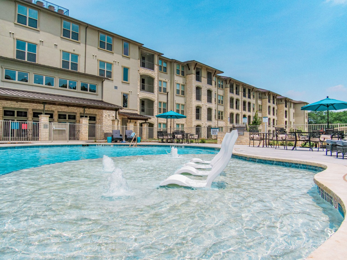 A luxurious apartment complex featuring a large outdoor pool with in-water lounge chairs and fountains.