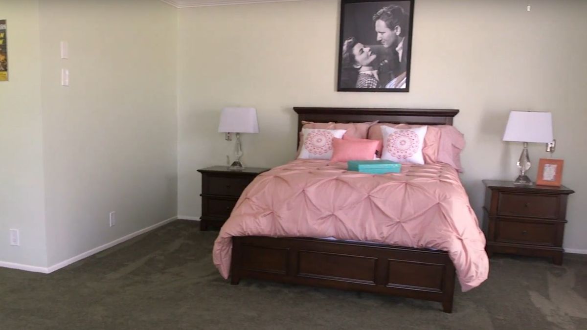 A cozy bedroom with a bed featuring pink bedding and decorative pillows, complemented by a nightstand and lamp.