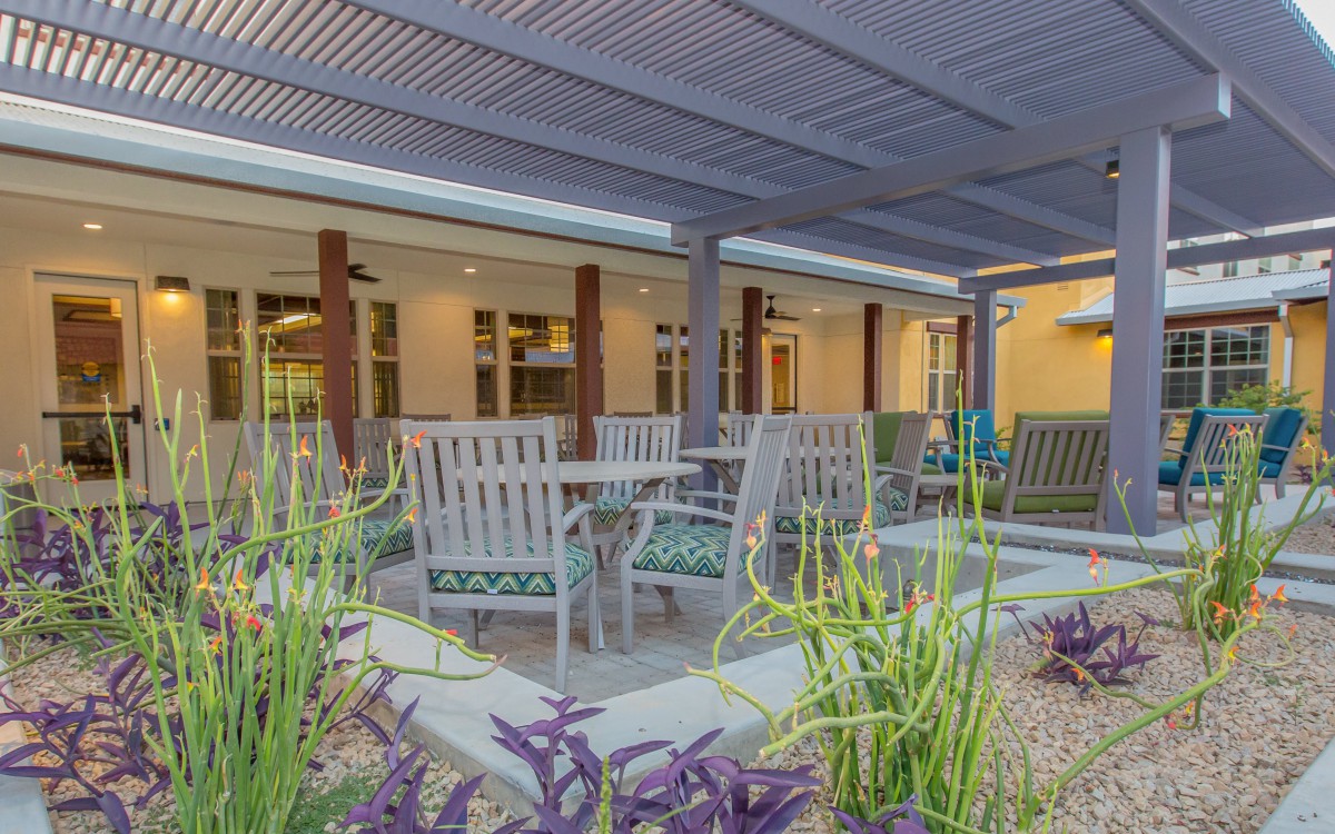 A cozy outdoor patio with seating under a pergola, surrounded by lush garden plants.
