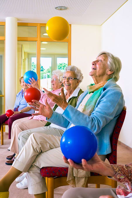 A group of seniors engaging in a fun indoor exercise activity with colorful balls.