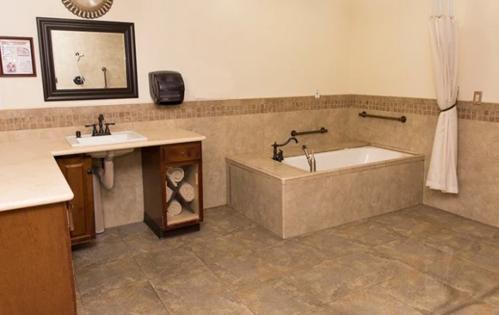 A spacious bathroom featuring a large bathtub with surrounding tiles, a sink with cabinet storage, and a wall-mounted mirror.