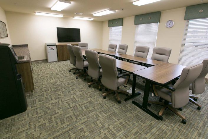 A well-lit conference room with a long table, several chairs, and a TV screen.