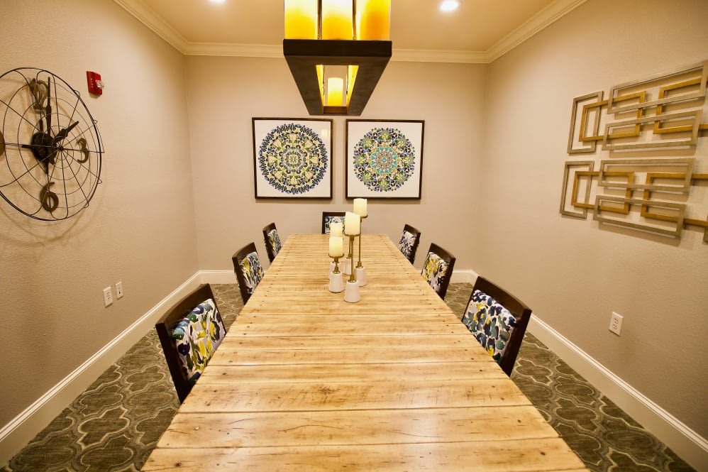 A modern dining room with a long wooden table, surrounded by chairs and decorated with candles and artwork on the walls.