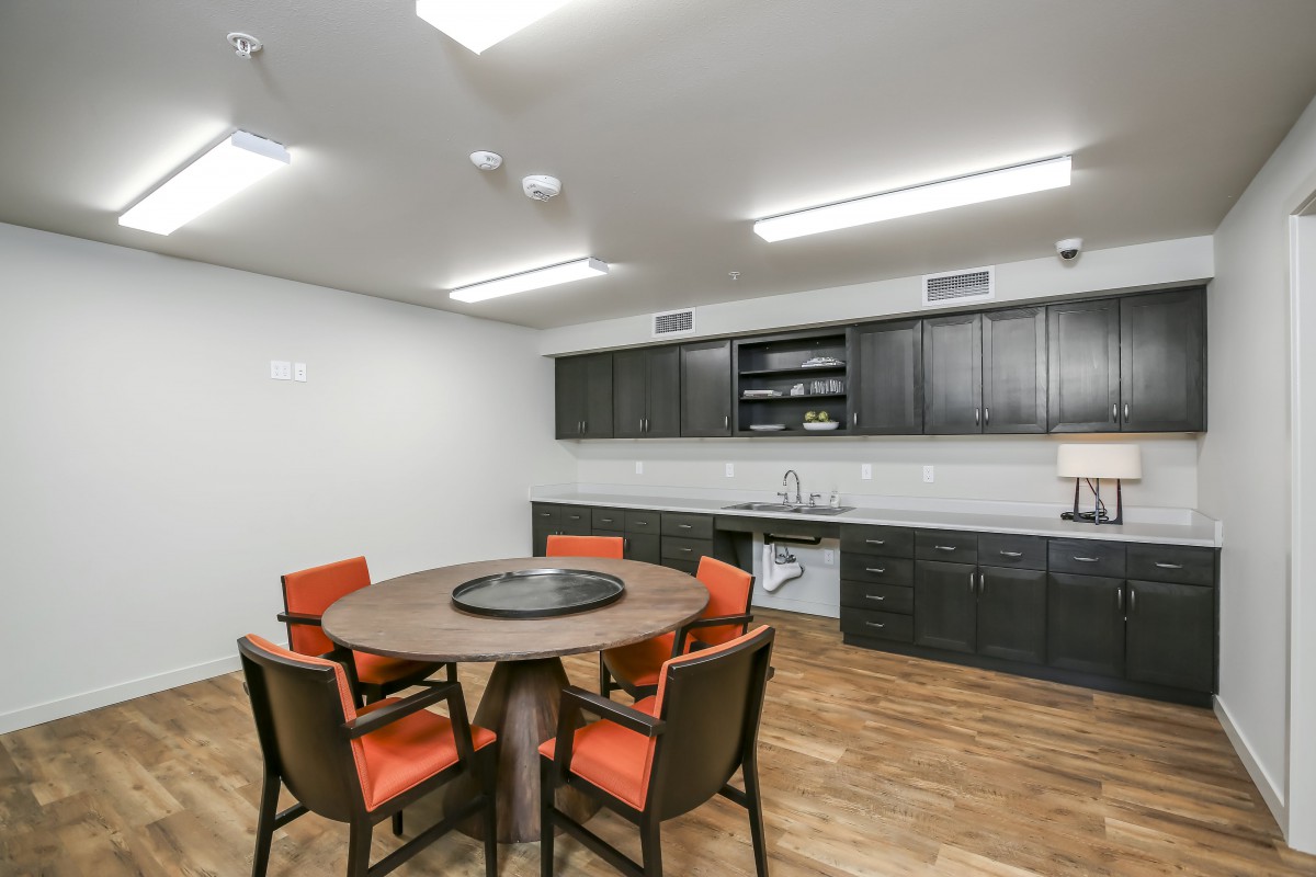 A modern kitchen and dining area featuring a round table with orange chairs, wood flooring, and sleek cabinetry.