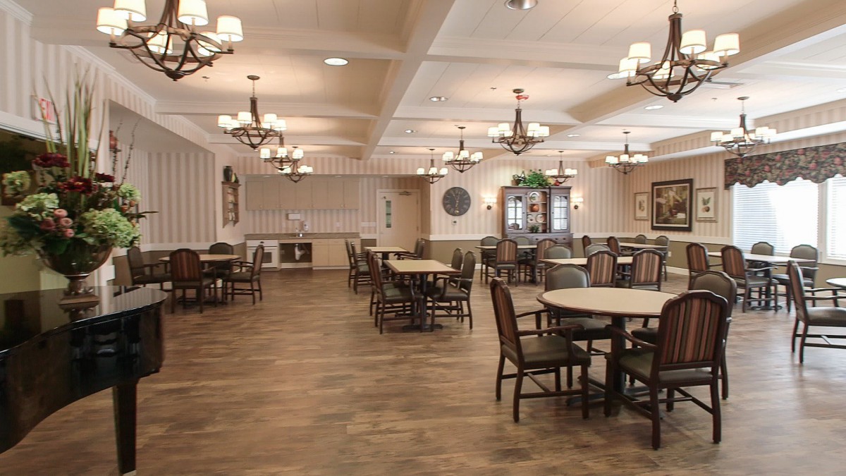 An elegantly decorated dining room with multiple tables and chairs, featuring chandeliers and wood flooring.