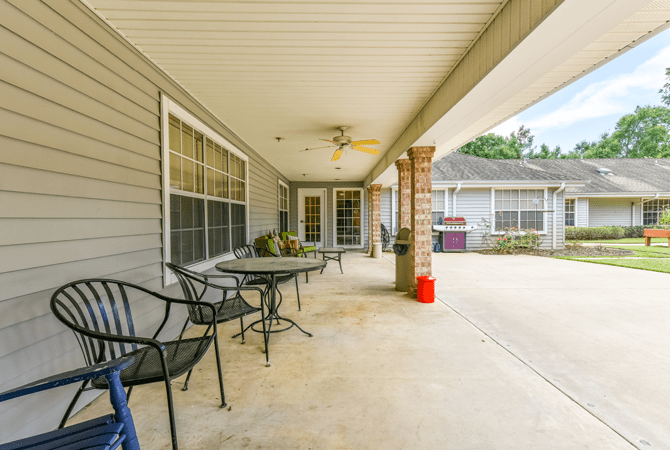 A spacious covered patio featuring chairs and a table, located at the back of a house.