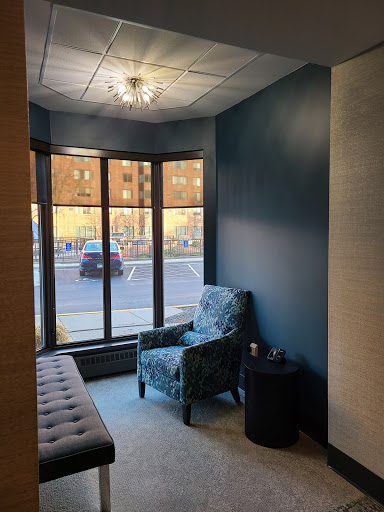A cozy waiting area with contemporary blue walls and a comfortable armchair, illuminated by natural light from large windows.