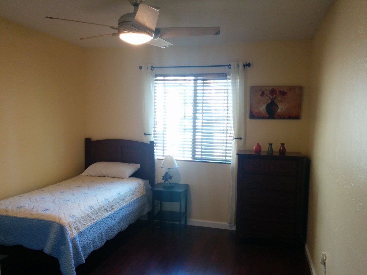 A cozy bedroom with a single bed, dresser, and a window letting in natural light.