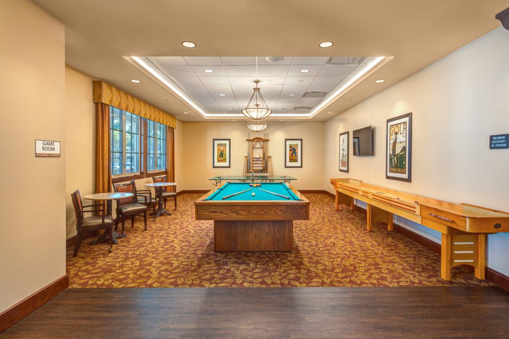 A well-lit game room featuring a pool table and shuffleboard, complemented by elegant decor and comfortable seating.