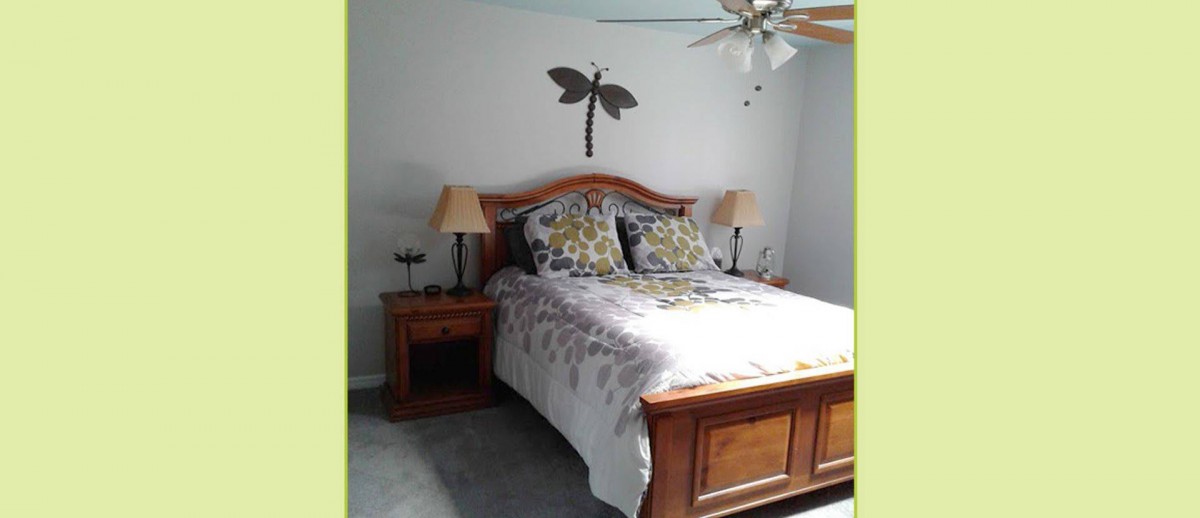 A cozy bedroom featuring a wooden bed with floral bedding, flanked by nightstands and a decorative dragonfly wall piece.