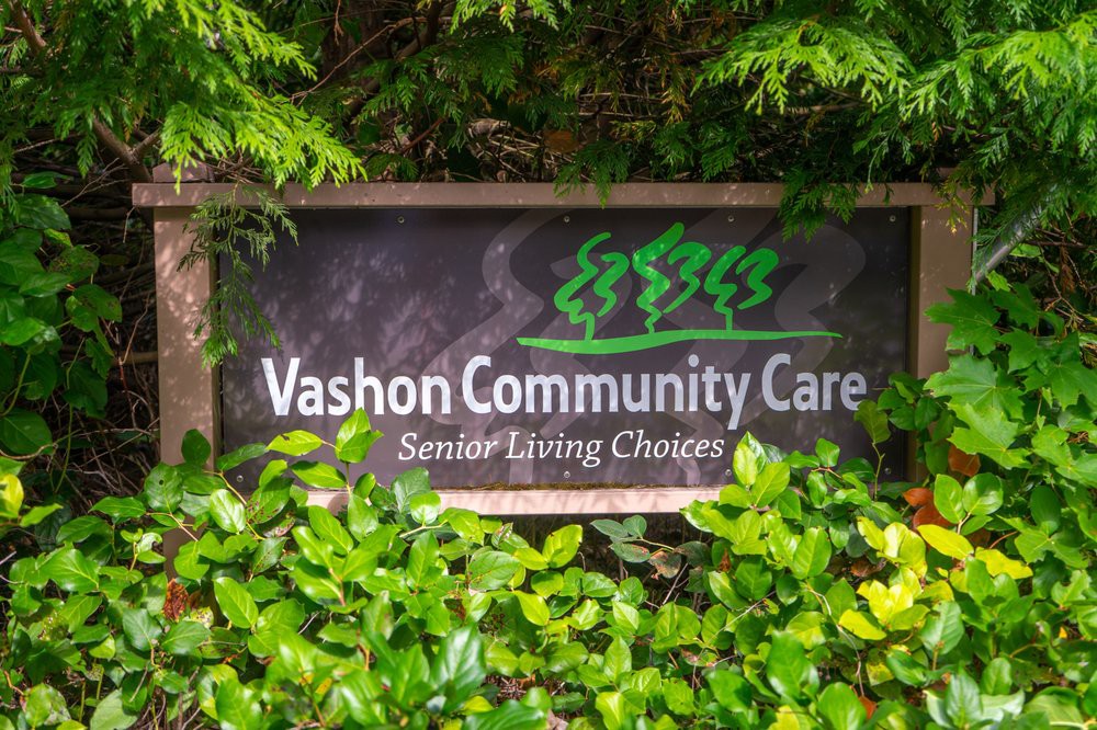 The sign for Vashon Community Care, surrounded by lush greenery.