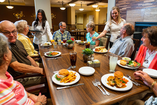 Seniors enjoying a meal together at a dining table, with attentive staff serving food.