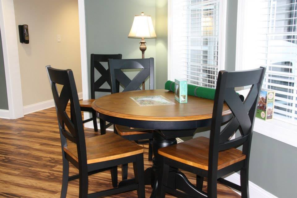 A cozy dining area featuring a round wooden table with black chairs and a lamp in the corner.