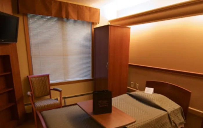 A hospital room with a bed, chair, and cabinet near a window.