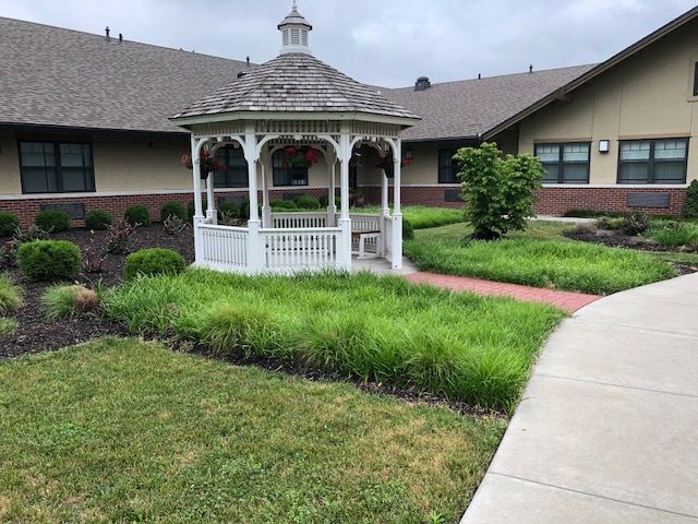 A scenic view of a white gazebo surrounded by a lush green garden and pathway.