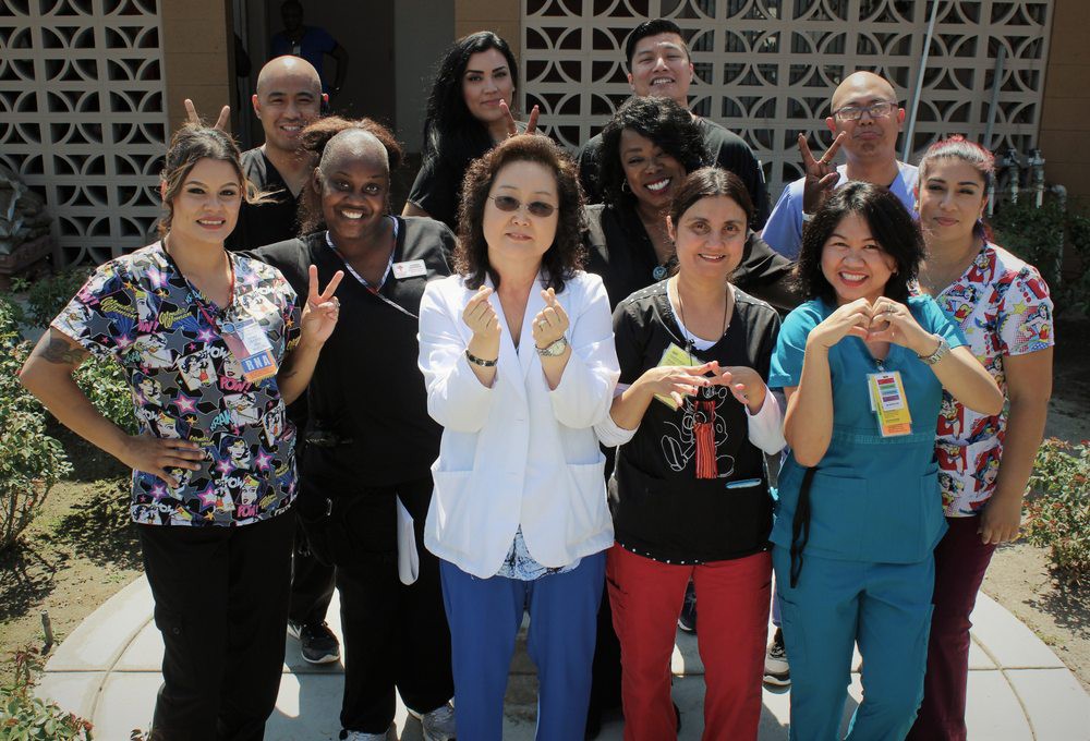A diverse group of people posing together outdoors, showing positive gestures and smiling.