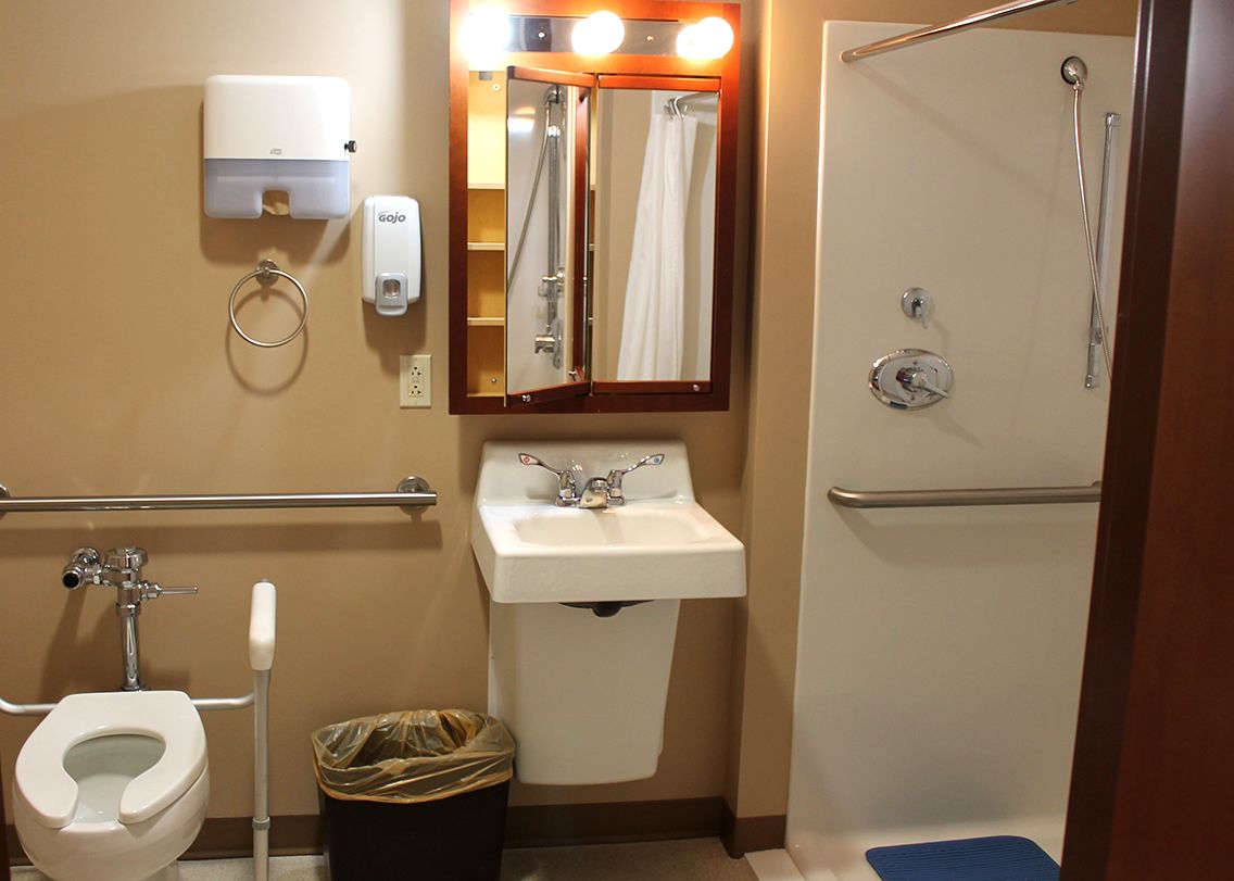 An accessible bathroom with a sink, mirror, and shower area equipped with handrails.