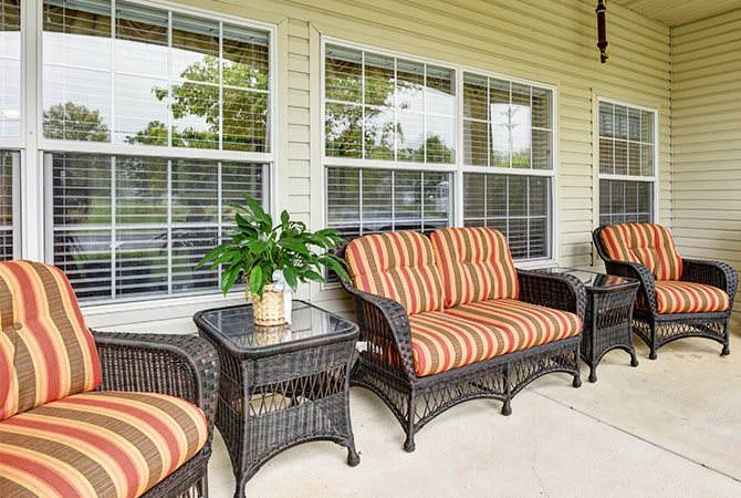 A cozy patio setup with wicker chairs and striped cushions, complemented by side tables and a potted plant in front of large windows.