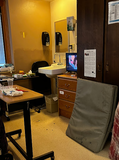 A view of a cluttered room featuring a desk, chair, and television.