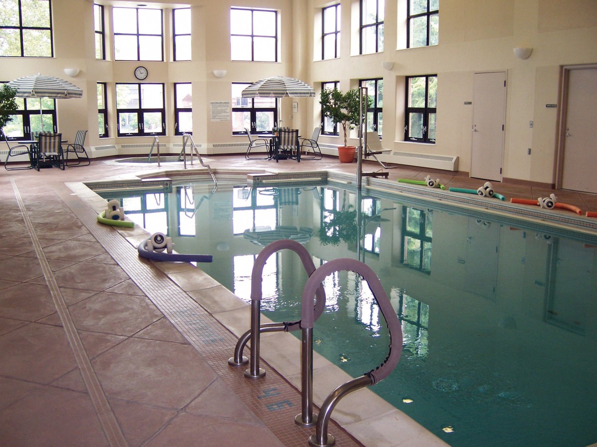 A serene indoor swimming pool with a ladder and windows overlooking the facility.