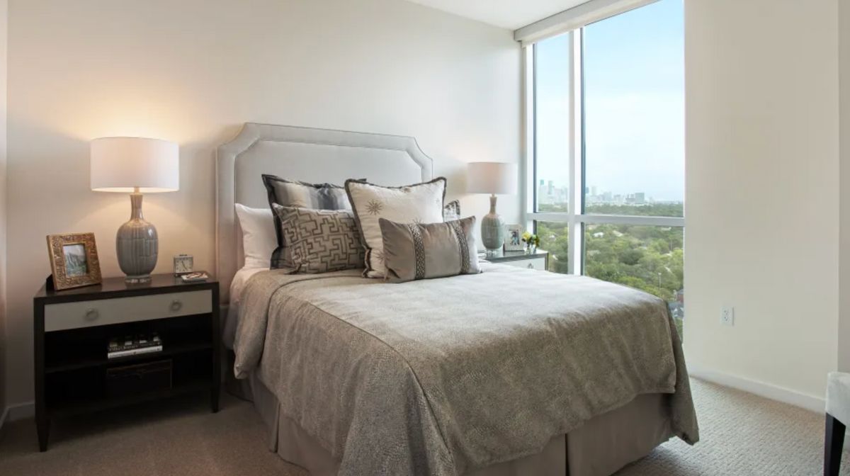 A modern and cozy bedroom with neutral tones, featuring a large window offering a scenic view.