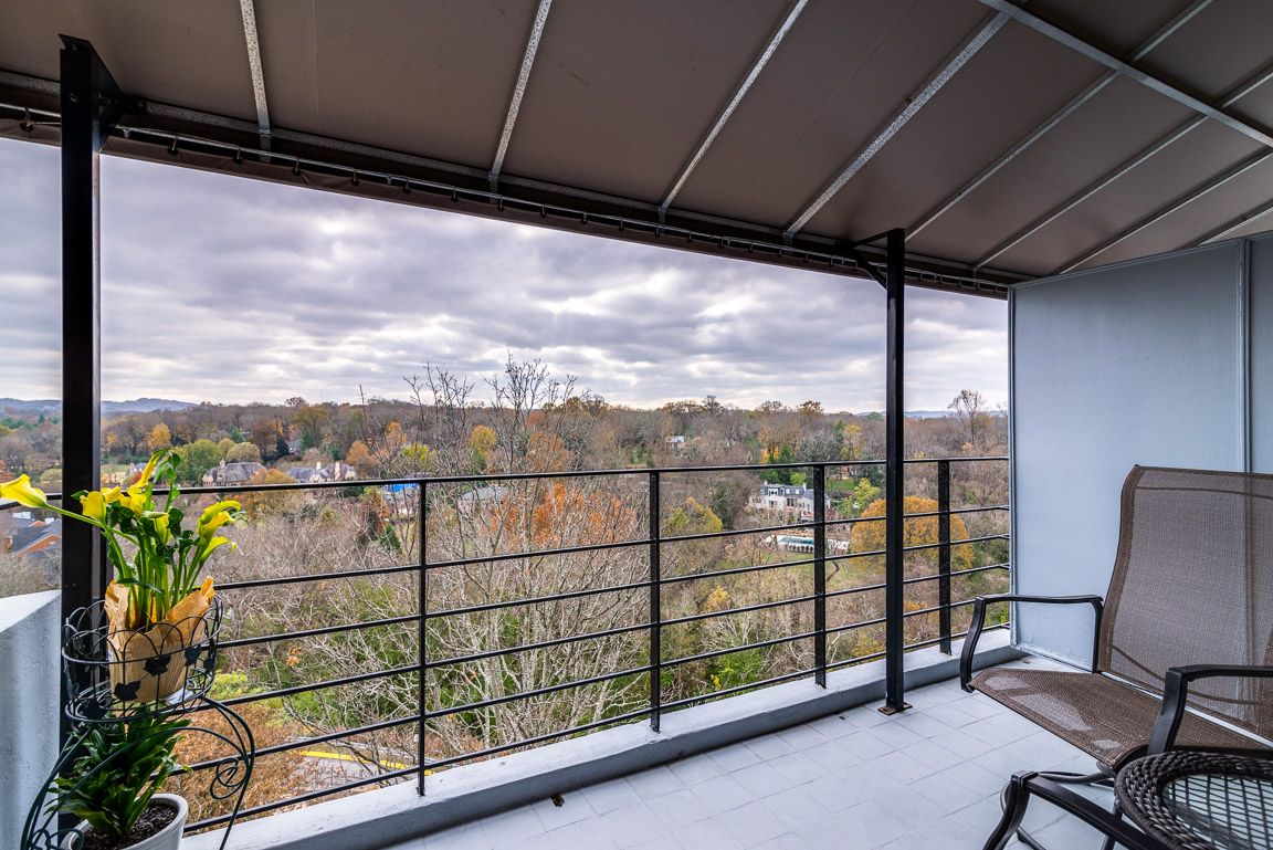 A spacious balcony with a metal railing overlooks a scenic landscape filled with autumn foliage under a cloudy sky.