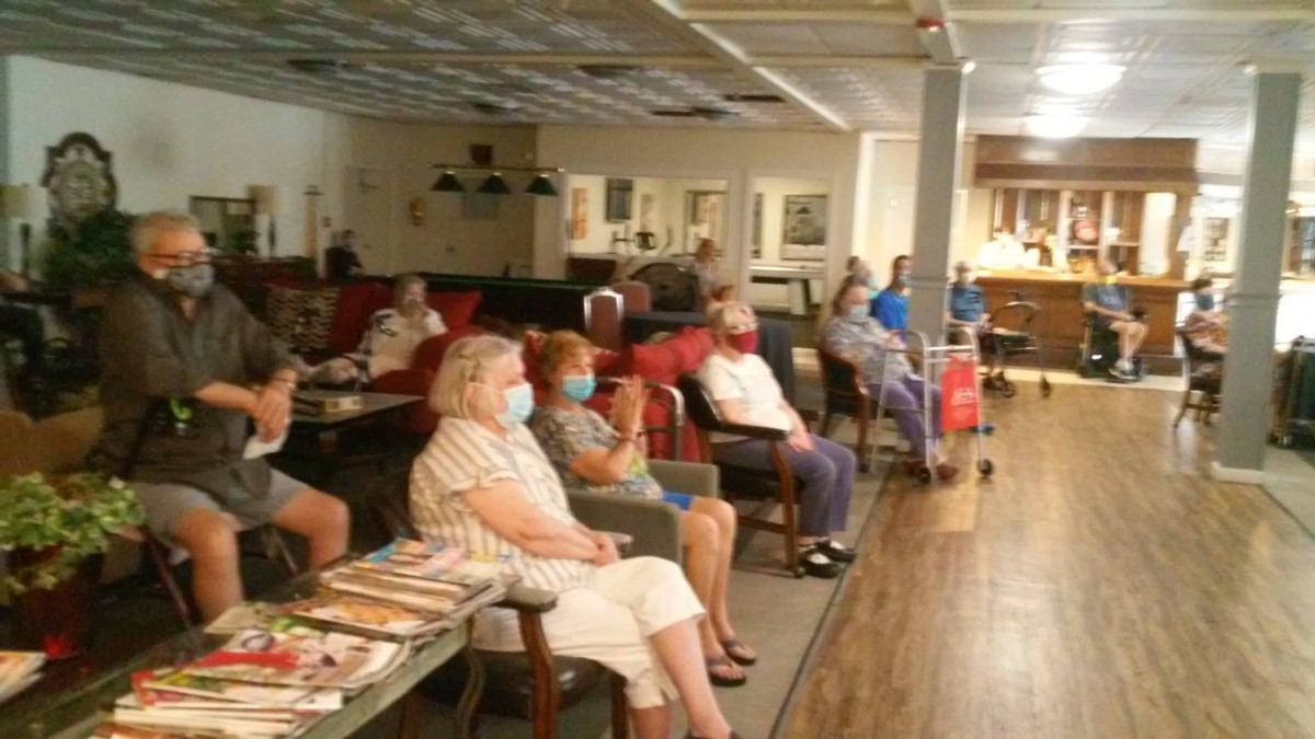 A group of senior citizens seated indoors, some wearing masks, in a community space.