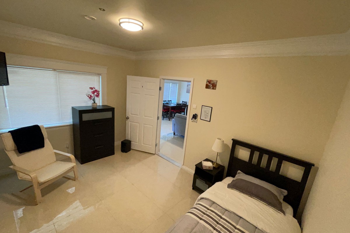 A cozy, minimalist bedroom with a bed, lamp, and window, featuring simple decor.