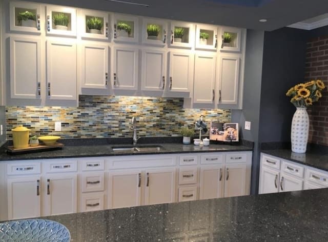 A modern kitchen featuring white cabinets, a dark countertop, and a decorative backsplash.