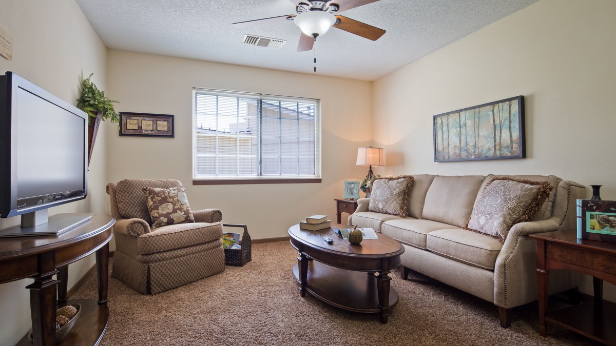 A cozy living room with a comfortable sofa, armchair, and coffee table, illuminated by a lamp and natural light from the window.