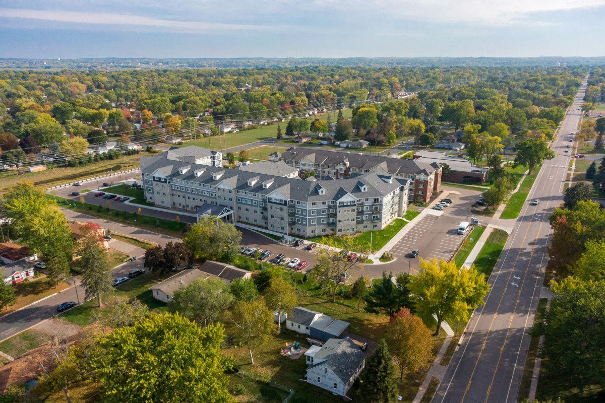 Aerial view of a residential building surrounded by trees and roads in an urban area.