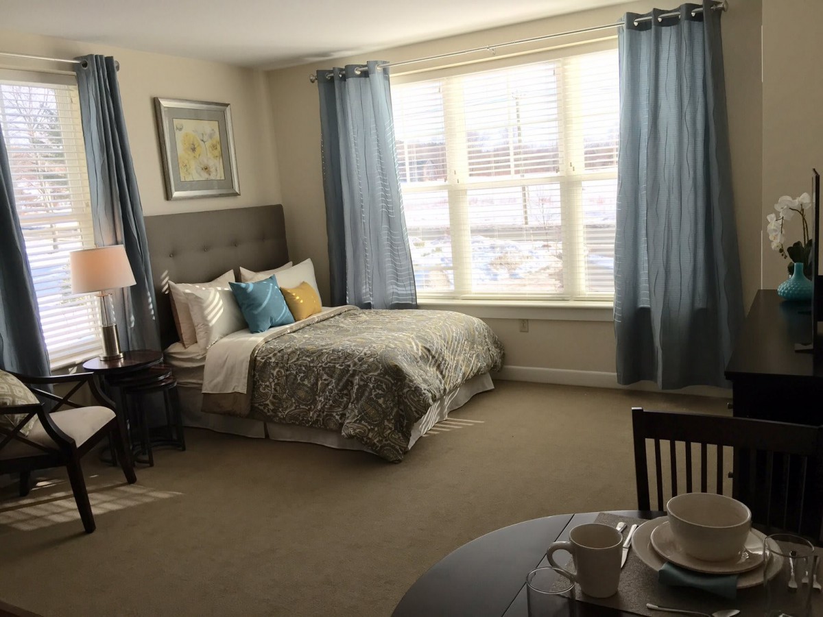 A cozy bedroom with a single bed, blue curtains, and natural lighting.