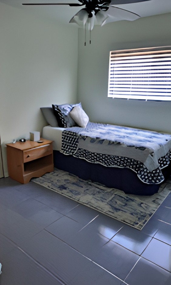 A minimalist bedroom with a single bed, nightstand, and window blinds.