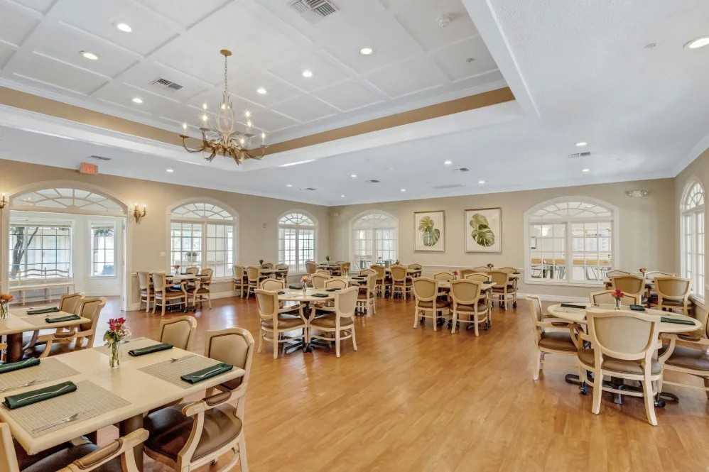A spacious dining room with wooden flooring, elegant chandeliers, and neatly arranged tables and chairs.