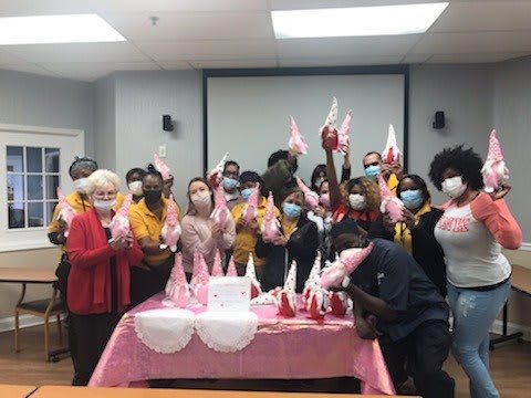 A group of people celebrating indoors with decorations, balloons, and a cake.