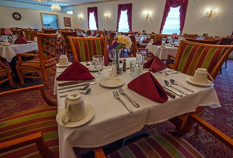 A formal dining room with elegantly set tables and vibrant red napkins.