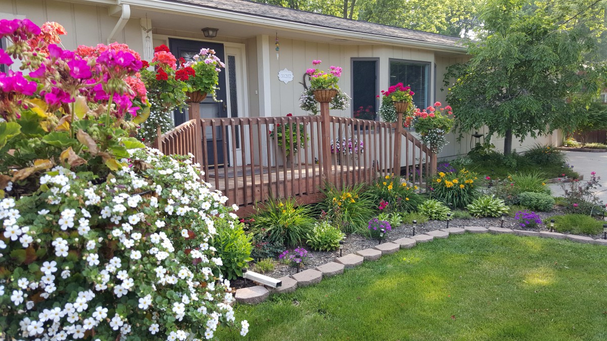 A well-maintained garden with vibrant flowers and a wooden deck in front of a house.